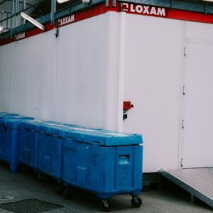 Outdoor recycling bins in a row beside a white building, promoting sustainability.