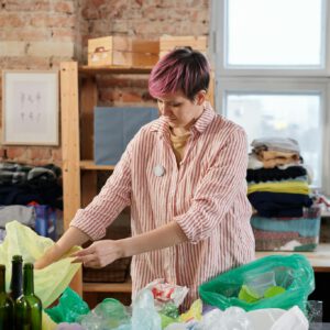 Woman organizing recyclables indoors, focusing on plastic and glass waste sorting for recycling efforts.
